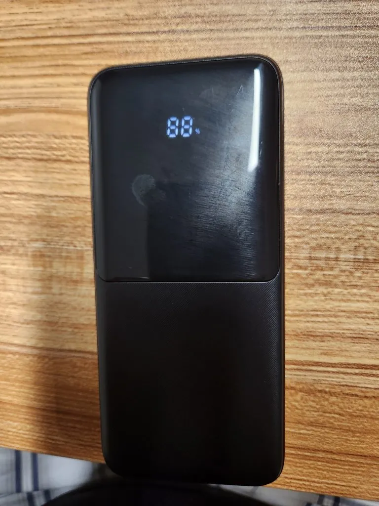 A black 15,000mAh power bank on a wooden table showing 88 percent on its LED display