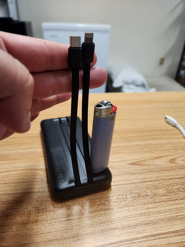 The power bank held in one hand with a cable pulled out, showing the compact size